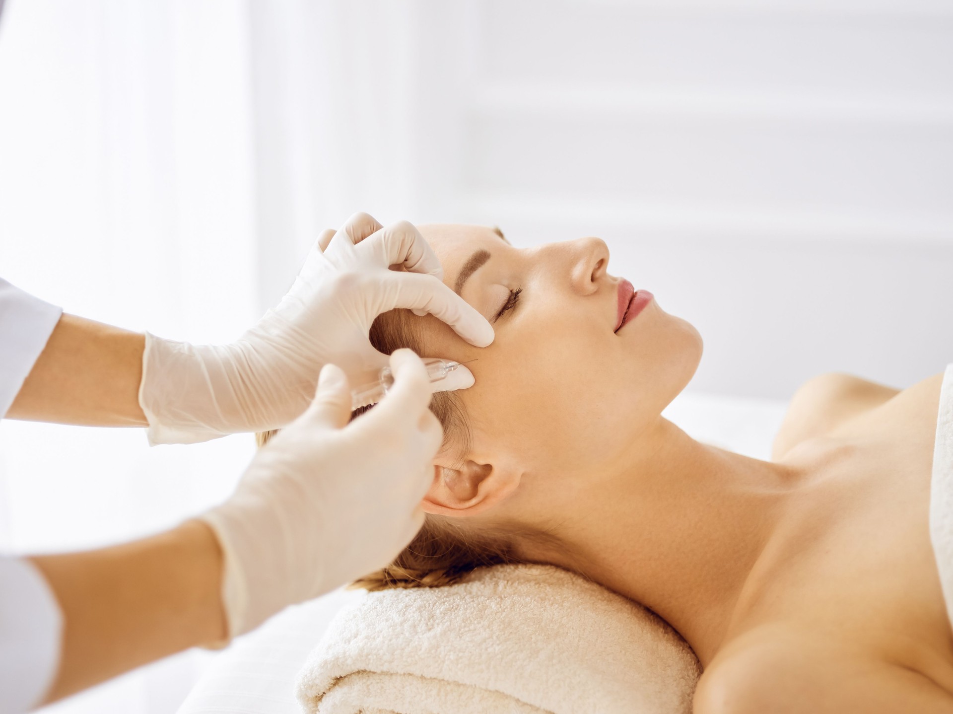 Beautiful woman receiving beauty injections with closed eyes. Beautician doctor hands doing beauty procedure to female face with syringe. Cosmetic medicine and surgery concept